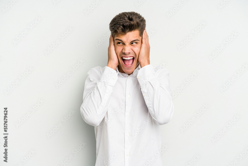 Young caucasian man isolated on white background covering ears with hands trying not to hear too loud sound. Young caucasian man isolated on white background covering ears with hands trying not to hear too loud sound.