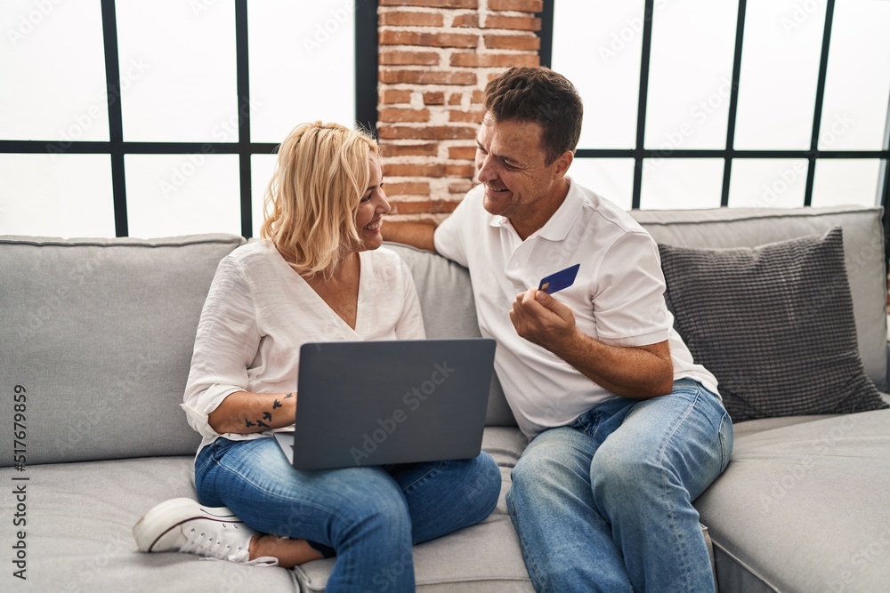 Middle age man and woman using laptop and credit card sitting on sofa at home Middle age man and woman using laptop and credit card sitting on sofa at home