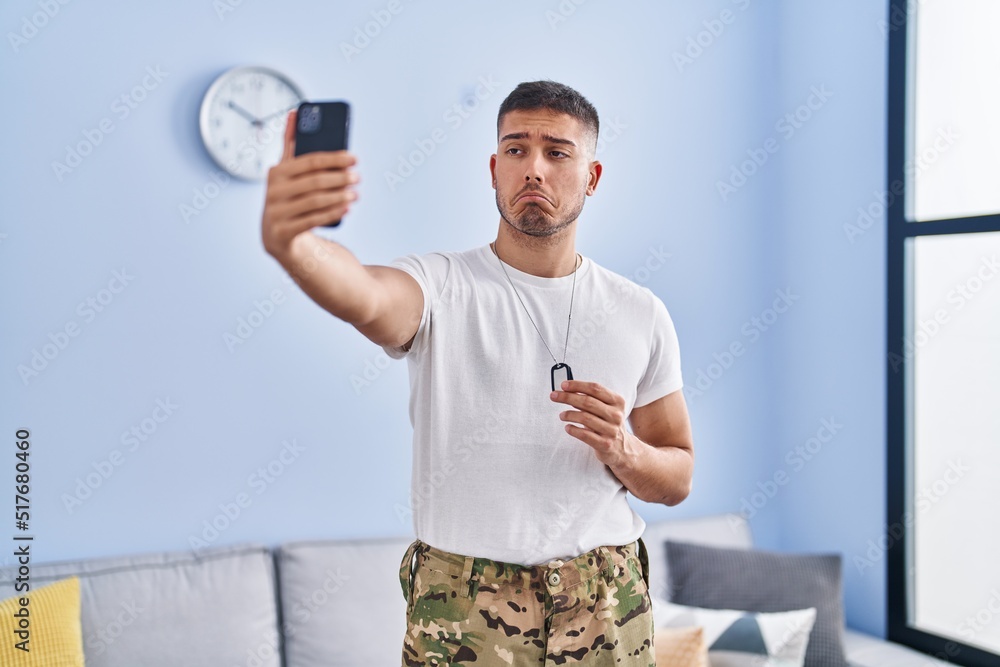 © Krakenimages.com - Young hispanic man wearing camouflage army uniform taking selfie at home depressed and worry for distress, crying angry and afraid. sad expression.