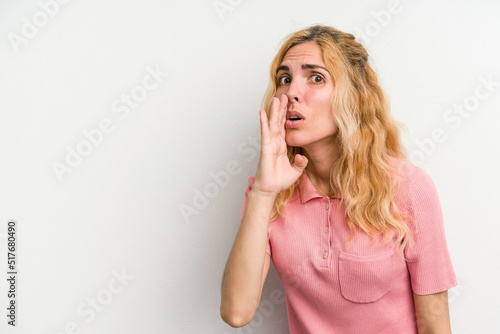 Young caucasian woman isolated on white background is saying a secret hot braking news and looking aside