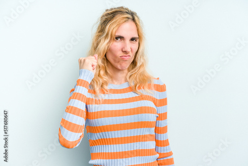 Young caucasian woman isolated on blue background showing fist to camera, aggressive facial expression.