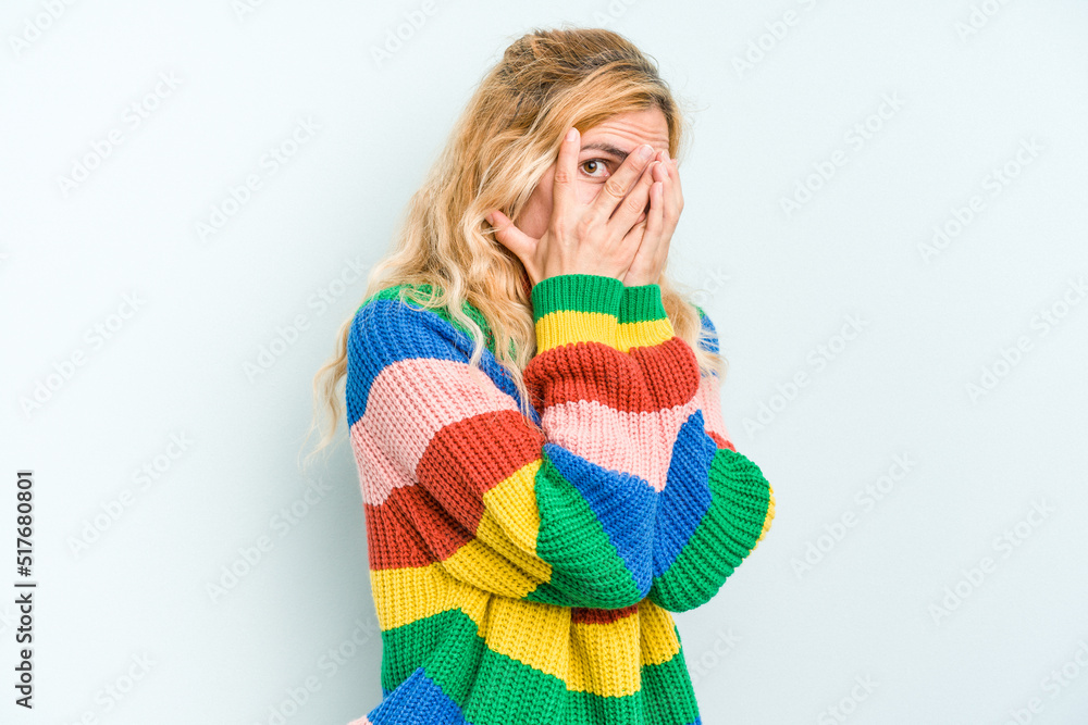 Young caucasian woman isolated on blue background blink through fingers frightened and nervous. Young caucasian woman isolated on blue background blink through fingers frightened and nervous.