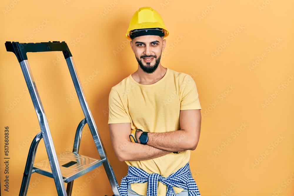 Handsome man with beard by construction stairs wearing hardhat happy face smiling with crossed arms looking at the camera. positive person. Handsome man with beard by construction stairs wearing hardhat happy face smiling with crossed arms looking at the camera. positive person.