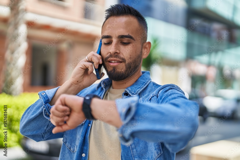 Young hispanic man talking on the smartphone looking watch at street Young hispanic man talking on the smartphone looking watch at street