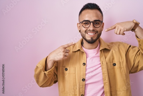Young hispanic man standing over pink background smiling cheerful showing and pointing with fingers teeth and mouth. dental health concept. © Krakenimages.com
