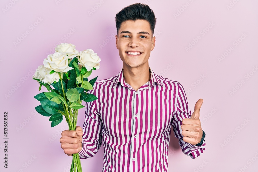 Young hispanic man holding flowers smiling happy and positive, thumb up doing excellent and approval sign Young hispanic man holding flowers smiling happy and positive, thumb up doing excellent and approval sign