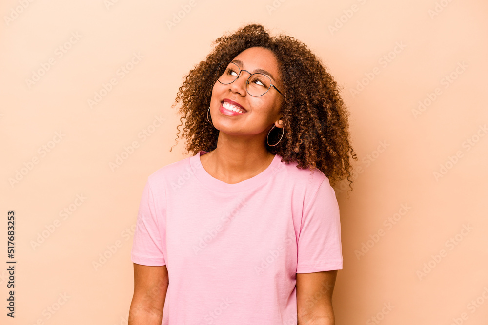 Young African American woman isolated on beige background relaxed and happy laughing, neck stretched showing teeth. Young African American woman isolated on beige background relaxed and happy laughing, neck stretched showing teeth.