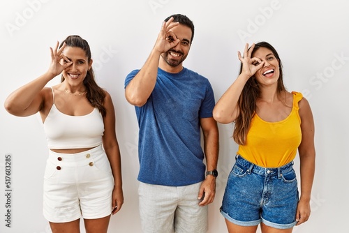 Group of young hispanic people standing over isolated background doing ok gesture with hand smiling  eye looking through fingers with happy face.