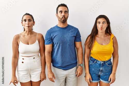 Group of young hispanic people standing over isolated background making fish face with lips  crazy and comical gesture. funny expression.
