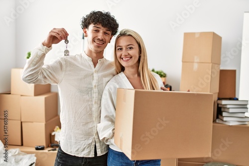 Young beautiful couple smiling happy holding cardboard box and key of new home.