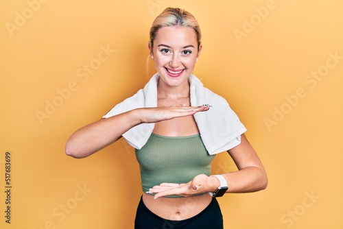 Young blonde girl wearing sportswear and towel gesturing with hands showing big and large size sign, measure symbol. smiling looking at the camera. measuring concept. © Krakenimages.com