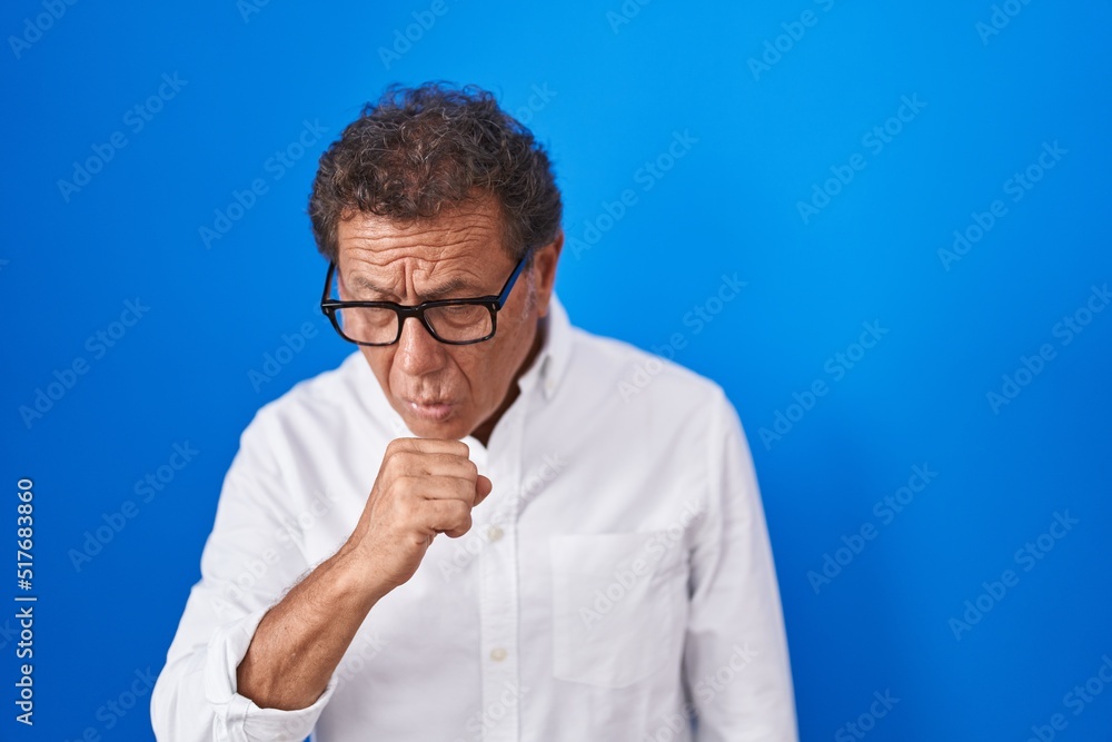 Middle age hispanic man standing over blue background feeling unwell and coughing as symptom for cold or bronchitis. health care concept.