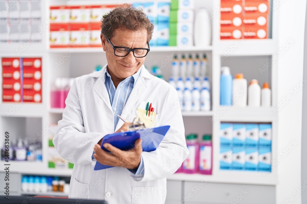 Middle age man pharmacist smiling confident writing on clipboard at pharmacy