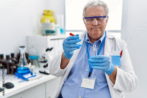 Middle age grey-haired man wearing scientist uniform using pipette at laboratory