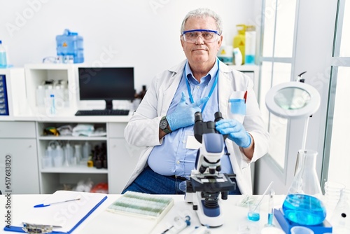 Senior caucasian man working at scientist laboratory cheerful with a smile on face pointing with hand and finger up to the side with happy and natural expression