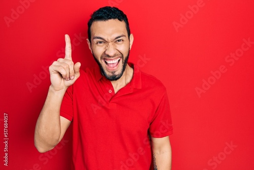 Hispanic man with beard wearing casual red t shirt pointing finger up with successful idea. exited and happy. number one.