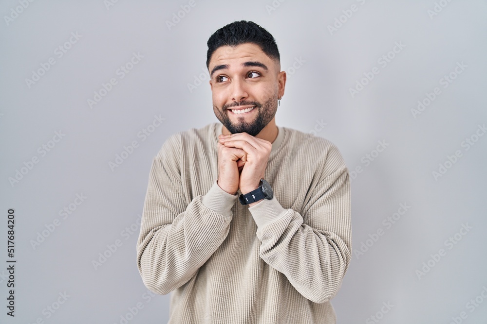 Young handsome man standing over isolated background laughing nervous and excited with hands on chin looking to the side Young handsome man standing over isolated background laughing nervous and excited with hands on chin looking to the side
