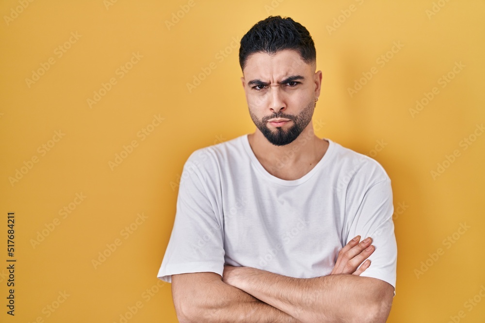 Young handsome man wearing casual t shirt over yellow background skeptic and nervous, disapproving expression on face with crossed arms. negative person. Young handsome man wearing casual t shirt over yellow background skeptic and nervous, disapproving expression on face with crossed arms. negative person.