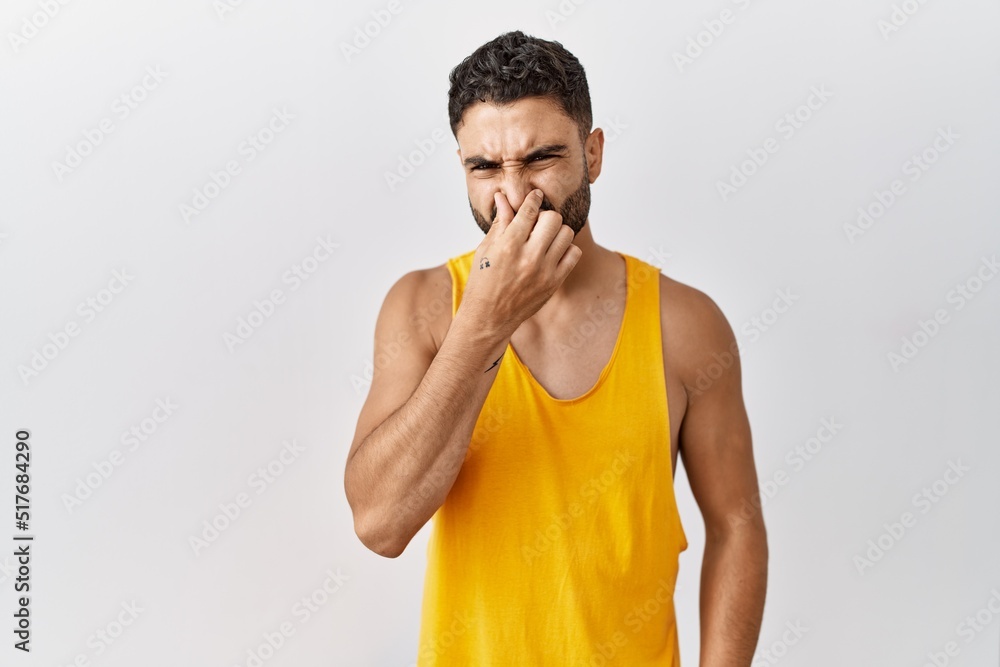 Young handsome man with beard standing over isolated background smelling something stinky and disgusting, intolerable smell, holding breath with fingers on nose. bad smell Young handsome man with beard standing over isolated background smelling something stinky and disgusting, intolerable smell, holding breath with fingers on nose. bad smell