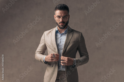 Fototapeta confident young man with glasses closing elegant suit and being cool