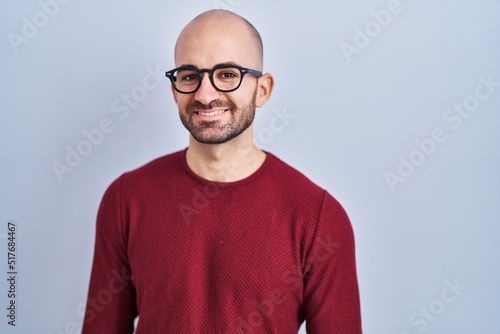 Young bald man with beard standing over white background wearing glasses with a happy and cool smile on face. lucky person. © Krakenimages.com