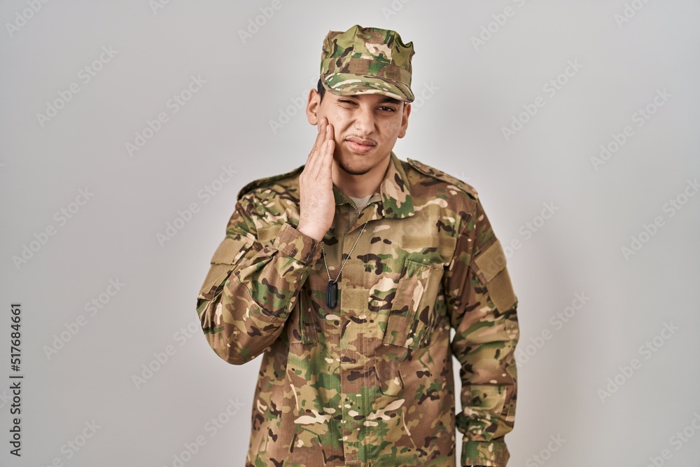 Young arab man wearing camouflage army uniform touching mouth with hand with painful expression because of toothache or dental illness on teeth. dentist Young arab man wearing camouflage army uniform touching mouth with hand with painful expression because of toothache or dental illness on teeth. dentist