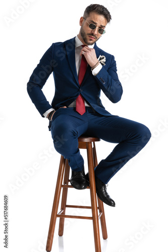 sexy man in elegant suit with sunglasses adjusting tie