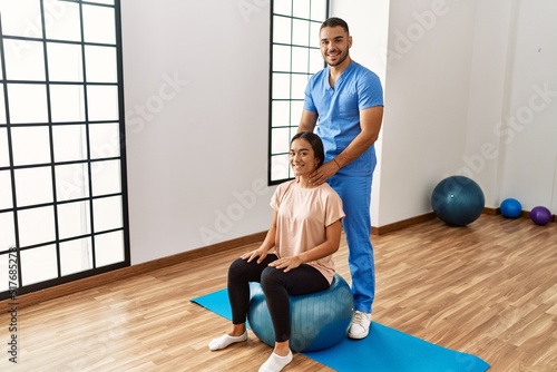 Latin man and woman wearing physiotherapist uniform using fit ball massaging neck at rehab center