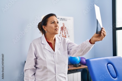 Middle age hispanic woman physiotherapist holding radiography at rehab clinic