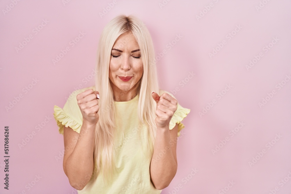 Caucasian woman standing over pink background excited for success with arms raised and eyes closed celebrating victory smiling. winner concept. Caucasian woman standing over pink background excited for success with arms raised and eyes closed celebrating victory smiling. winner concept.