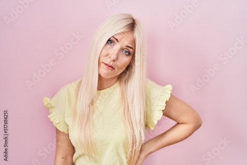 Caucasian woman standing over pink background looking sleepy and tired, exhausted for fatigue and hangover, lazy eyes in the morning.