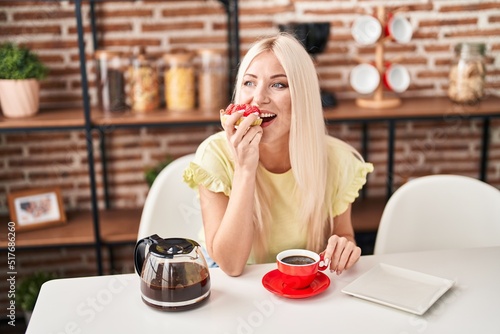 Young blonde woman having breakfast sitting on table at home