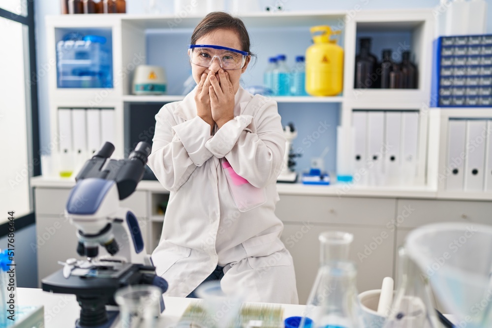 Hispanic girl with down syndrome working at scientist laboratory laughing and embarrassed giggle covering mouth with hands, gossip and scandal concept Hispanic girl with down syndrome working at scientist laboratory laughing and embarrassed giggle covering mouth with hands, gossip and scandal concept