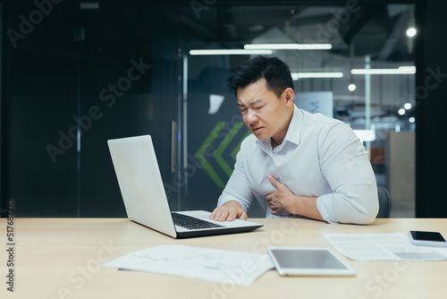 Sick Asian businessman at work, man chest pain heart, overworked and depressed boss.