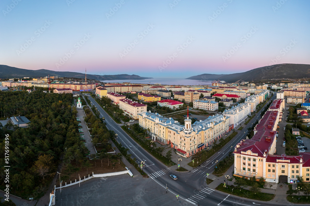 Aerial view of a seaside town. Top view of the streets and buildings. In the distance the sea bay and mountains. Beautiful morning cityscape. City of Magadan, Magadan region, Far East of Russia.