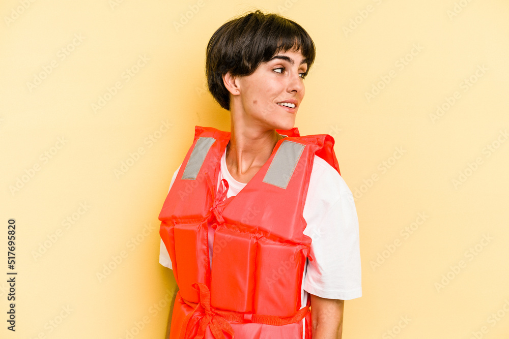 Young caucasian woman wearing life jacket isolated on yellow background looks aside smiling, cheerful and pleasant. Young caucasian woman wearing life jacket isolated on yellow background looks aside smiling, cheerful and pleasant.