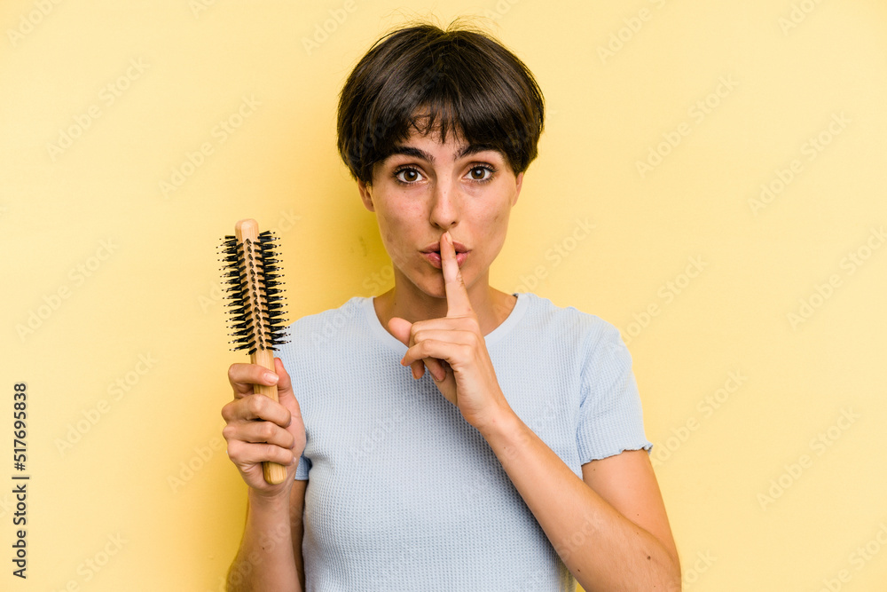 Young caucasian woman holding a brush hair isolated on yellow background keeping a secret or asking for silence. Young caucasian woman holding a brush hair isolated on yellow background keeping a secret or asking for silence.
