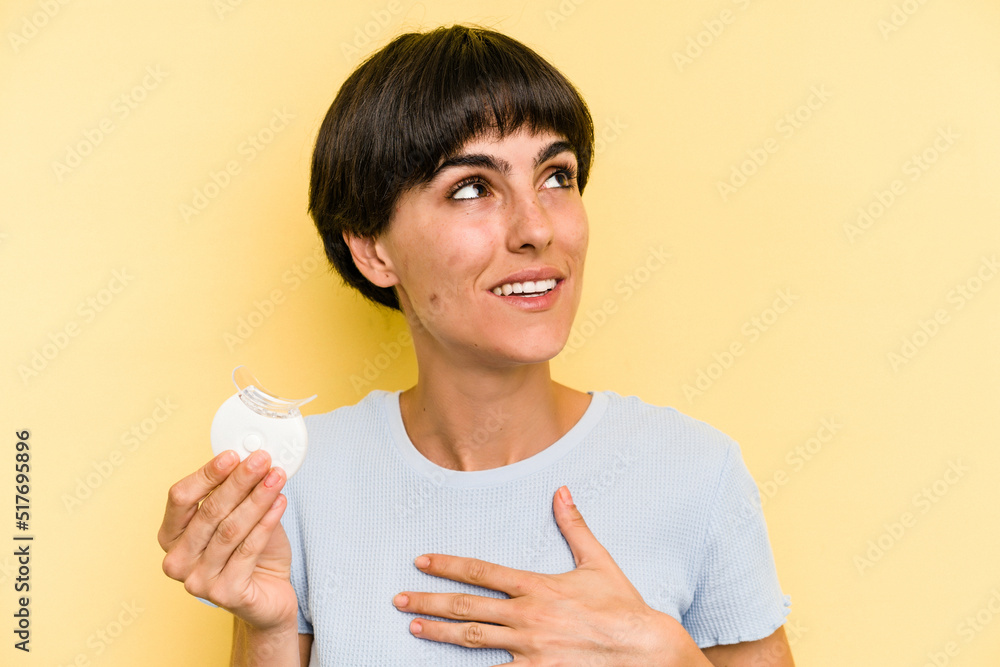 Young caucasian woman holding teeth whitener isolated on yellow background laughs out loudly keeping hand on chest. Young caucasian woman holding teeth whitener isolated on yellow background laughs out loudly keeping hand on chest.