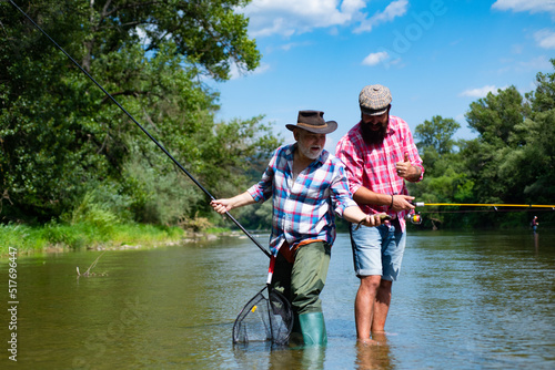 Foto Young and old fisherman standing on the shore of lake with fishing rod