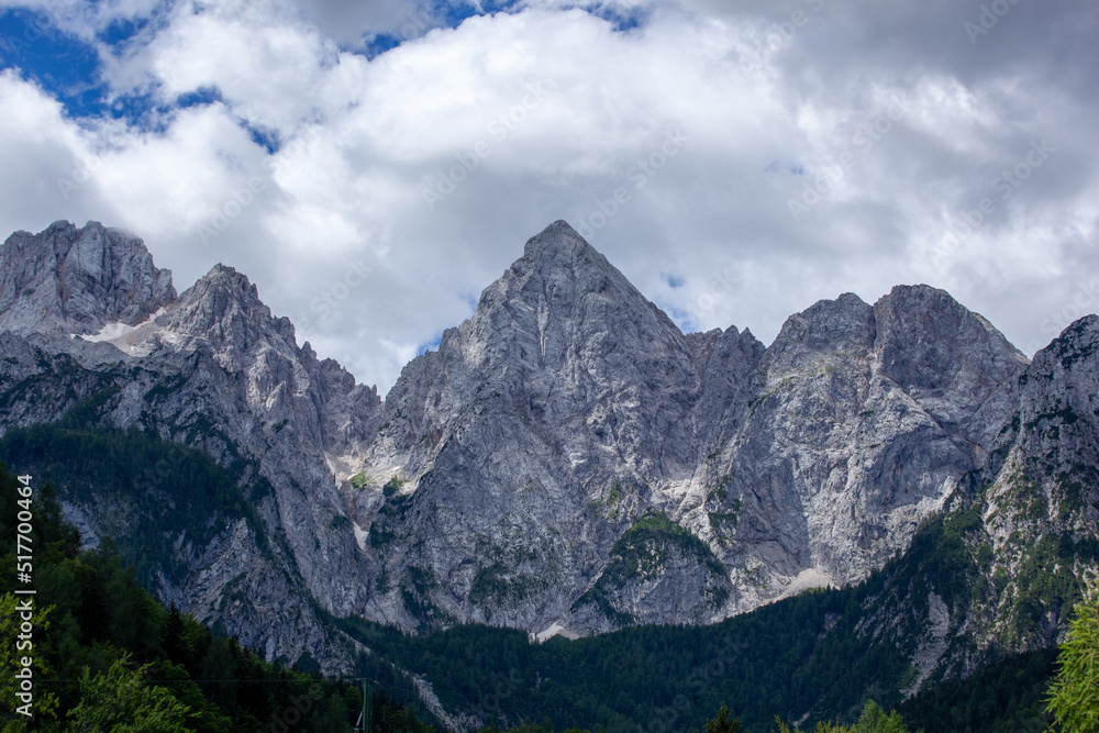 The peaks of Triglav National Park in Slovenia. The peaks are in the sun. The sky is overcast but shows blue skies. Spik Peak is clearly visible.