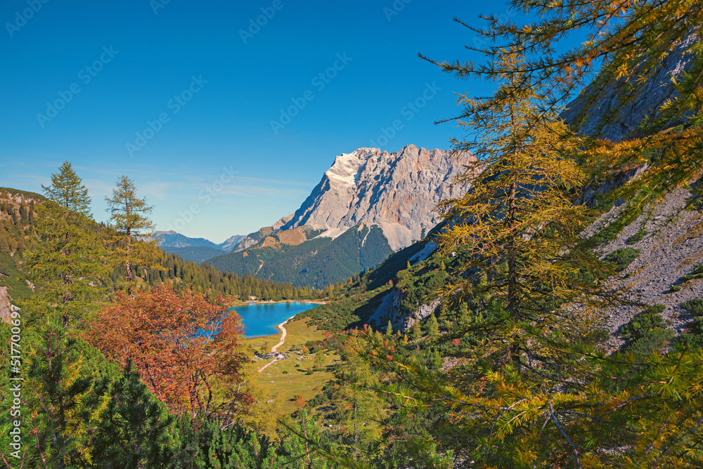 idyllic alpine landscape with lake view Seebensee, larch trees and forest in autumn