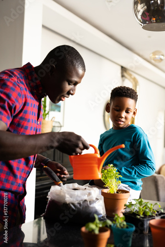 Image of smiling african american boy with father watering plant
