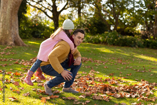 Image of happy caucasian father and daughter having fun in autumn leaves in garden