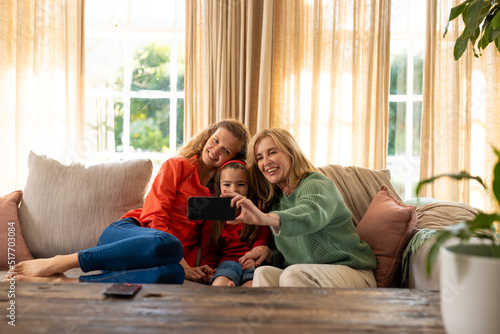 Image of happy three generation caucasian women sitting on sofa and taking selfie