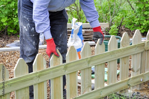 Background of hands of man in red and black gloves installing  a wooden fence in the garden and checking the level with a green string over the wooden fence.