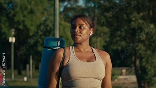 Plus size African-American woman walking with exercise mat through the park in a summer day