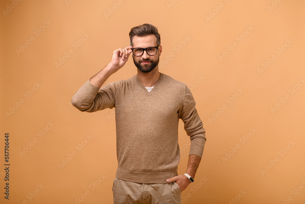 Charismatic bearded caucasian handsome man isolated on beige background standing and looks at the camera, male entrepreneur in casual wear adjusting stylish eyeglasses Charismatic bearded caucasian handsome man isolated on beige background standing and looks at the camera, male entrepreneur in casual wear adjusting stylish eyeglasses