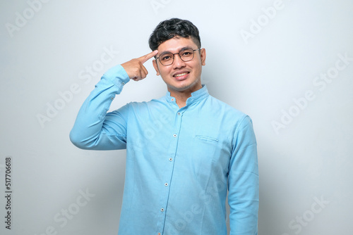 Young asian man wearing casual shirt smiling pointing to head with both hands finger, great idea or thought.