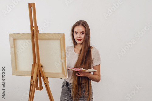 ?ute girl artist paints a picture on an easel with a brush and paints