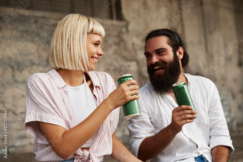 Closeup of young smiling couple toasting with beer cans in an urban environment